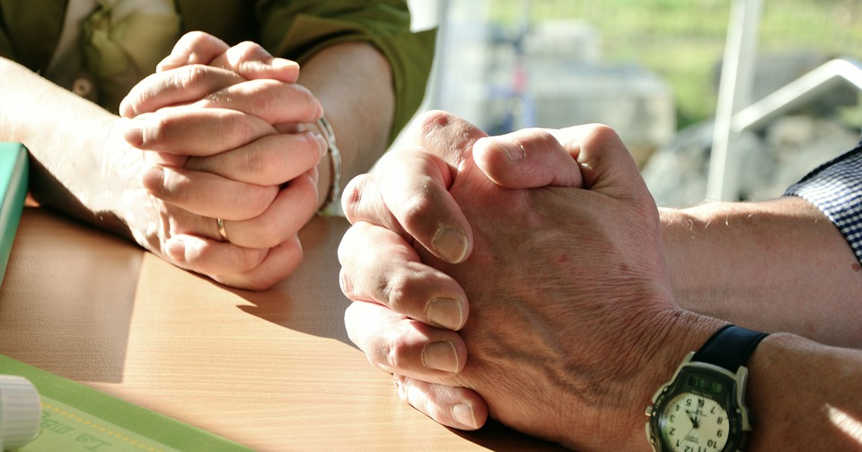 Two hands are folded in prayer.